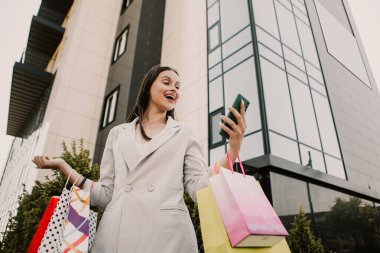 Shocked lady hold hands many bags and phone shopper woman dressed plaid blazer carrying enjoying new clothes packs things after shopping buyings sales black friday concept