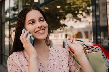 Lady hold many bags and talking with friend on the phone shopper woman dressed pink flower pattern dress carrying enjoying new clothes packs things after shopping buyings sales black friday concept