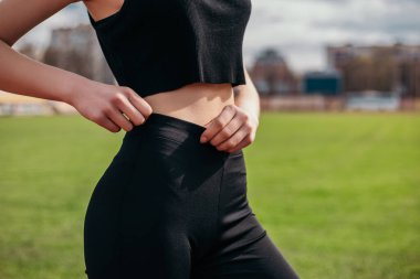 Slim woman standing posing showing body abdominal press muscles outside stadium morning looking away. Athletic lady dressed fitness sportwear clothes. Healthy lifestyle sport recreation. Copy space