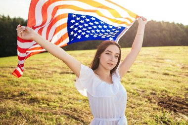 4 Temmuz kutlu olsun! Bağımsızlık Günü kutlaması. Vatansever kadın Amerikan bayrağına sarılmış rüzgarda sallanıyor ve sahada yürüyor. Yıldızlar ve çizgiler. Özgürlük kavramı.