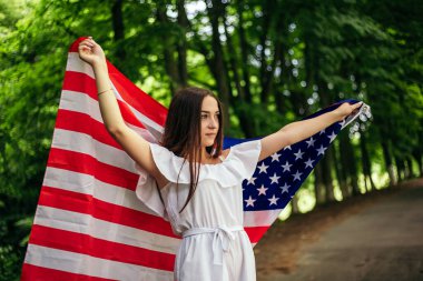 4 Temmuz kutlu olsun! Bağımsızlık Günü kutlaması. Vatansever kadın Amerikan bayrağına sarılmış rüzgarda sallanıyor ve yolda yürüyor. Yıldızlar ve çizgiler. Özgürlük kavramı.