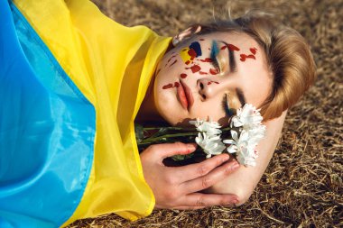 Ukrayna 'nın yanında dur! Ukrayna sarısı mavi bayrağa sarılmış bir kadın yerde yatıyor. Ukrayna 'nın ulusal sembolü. Kan makyajlı kadın papatya çiçeği tutar. Destek ve dayanışma. 