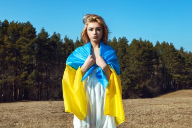 Ukrayna sarısı mavi bayrağa sarılı kadın portresi rüzgarda dalgalanıyor. Ukrayna 'nın ulusal sembolü. Makyajlı vatansever kadın sahada yürüyor. Ukrayna, destek ve dayanışma