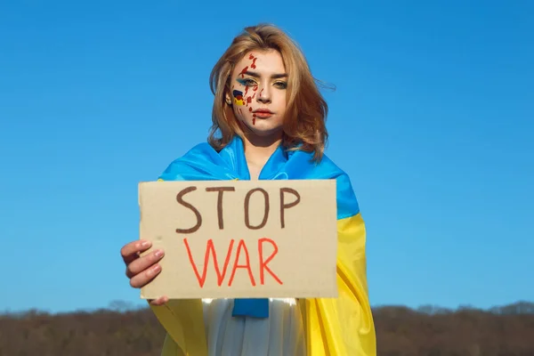 Savaşı durdurun! Ukrayna sarısı mavi bayrağa sarılı protesto işareti olan bir kadın. Ukrayna 'nın ulusal sembolü. Kan makyajlı kadın vatansever bir isim plakası taşıyor. Ukrayna, destek ve dayanışma. 