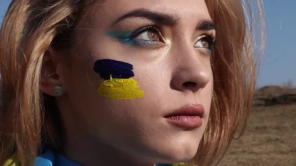 用乌克兰语黄色蓝色旗帜包裹的女人 乌克兰的国徽在脸颊上 有妆容的爱国女士与乌克兰站在一起 支持和声援 — 图库视频影像