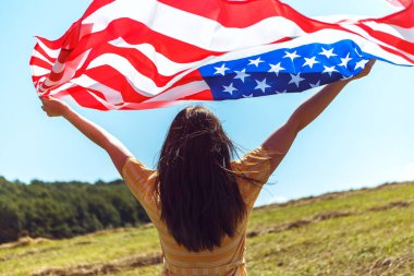 4 Temmuz kutlu olsun! Bağımsızlık Günü kutlaması. Vatansever kadın Amerikan bayrağına sarılmış rüzgarda sallanıyor ve sahada yürüyor. Yıldızlar ve çizgiler. Özgürlük kavramı.