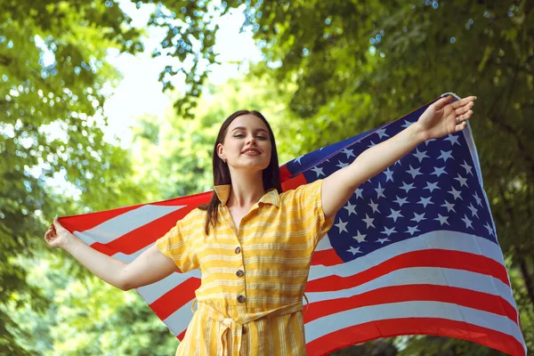 4 Temmuz kutlu olsun! Bağımsızlık Günü kutlaması. Vatansever kadın Amerikan bayrağına sarılmış rüzgarda sallanıyor ve yolda yürüyor. Yıldızlar ve çizgiler. Özgürlük kavramı.