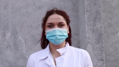 Yavaş çekim. Caddede yürüyen hemşire. Mavi tek kullanımlık maske ve eldiven takmış, beyaz elbiseli bir kadın doktor..