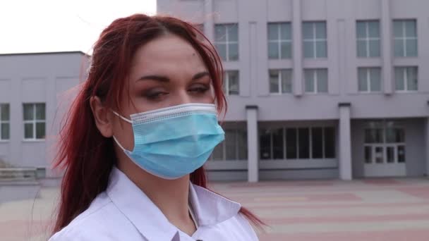 慢镜头 护士站在医院附近的街上 看着摄像机 女医生身穿医用白衣 戴着蓝色一次性口罩和手套 — 图库视频影像
