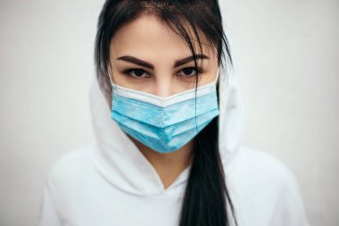 Beyaz kapüşonlu kadın mavi bir maske takıyor. Kameraya bakan kadın, yeni mutasyona uğrayan Coronavirus hastalığı önleme salgını sağlık riski konsepti