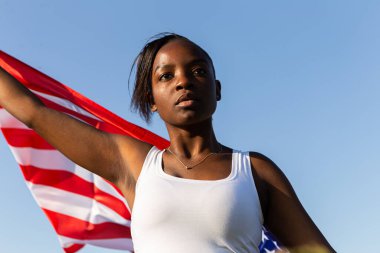 Amerikan bayrağına sarılmış Afro-Amerikalı kadın rüzgarda dalgalanıyor. 4 Temmuz kutlu olsun! Bağımsızlık Günü kutlaması. Yıldızlar ve çizgiler. Özgürlük kavramı.