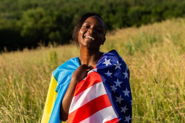 Afro-Amerikan kadın Amerikan bayrağına sarılmış ve rüzgarda dalgalanan Ukrayna bayrağı. Ukrayna, uluslararası destek ve dayanışma. Özgürlük kavramı.