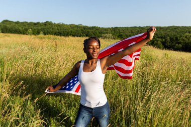 Amerikan bayrağına sarılmış Afro-Amerikalı kadın rüzgarda dalgalanıyor. 4 Temmuz kutlu olsun! Bağımsızlık Günü kutlaması. Yıldızlar ve çizgiler. Özgürlük kavramı.