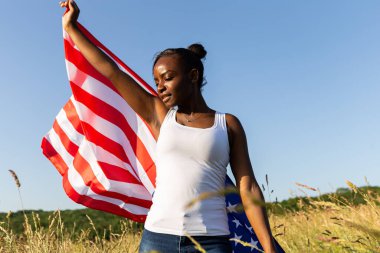 Amerikan bayrağına sarılmış Afro-Amerikalı kadın rüzgarda dalgalanıyor. 4 Temmuz kutlu olsun! Bağımsızlık Günü kutlaması. Yıldızlar ve çizgiler. Özgürlük kavramı.