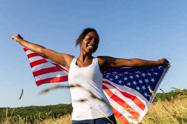 Amerikan bayrağına sarılmış Afro-Amerikalı kadın rüzgarda dalgalanıyor. 4 Temmuz kutlu olsun! Bağımsızlık Günü kutlaması. Yıldızlar ve çizgiler. Özgürlük kavramı.