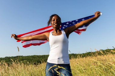 Amerikan bayrağına sarılmış Afro-Amerikalı kadın rüzgarda dalgalanıyor. 4 Temmuz kutlu olsun! Bağımsızlık Günü kutlaması. Yıldızlar ve çizgiler. Özgürlük kavramı.