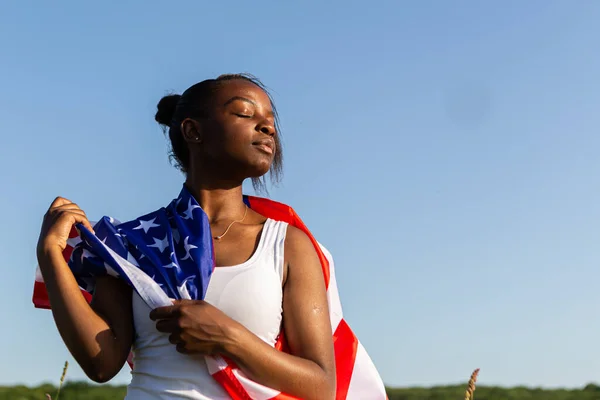 African american woman wrapped in american flag flutters waving in the wind. Happy 4th of July! Independence Day celebrating. Stars and stripes. Freedom concept.