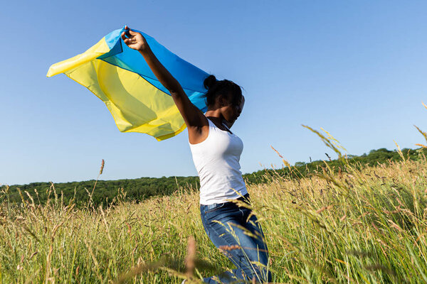 Африканская американка, завернутая в украинский желтый флаг, развевается на ветру. Национальный символ Украины. Стоять с Украиной, международная поддержка и солидарность