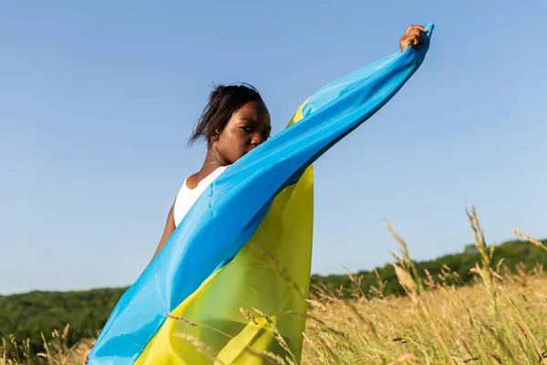 アフリカ系アメリカ人の女性は ウクライナの黄色の青い旗のフラッタ風に手を振って包まれた ウクライナの象徴 ウクライナとのスタンド 国際的な支援と連帯 — ストック写真