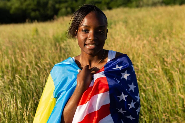 African american woman wrapped in american and ukrainian flag flutters waving in the wind. Stand with Ukraine, international support and solidarity. Freedom concept.