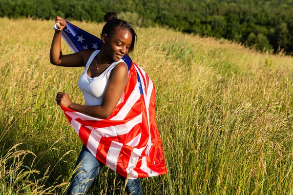 African american woman wrapped in american flag flutters waving in the wind. Happy 4th of July! Independence Day celebrating. Stars and stripes. Freedom concept.