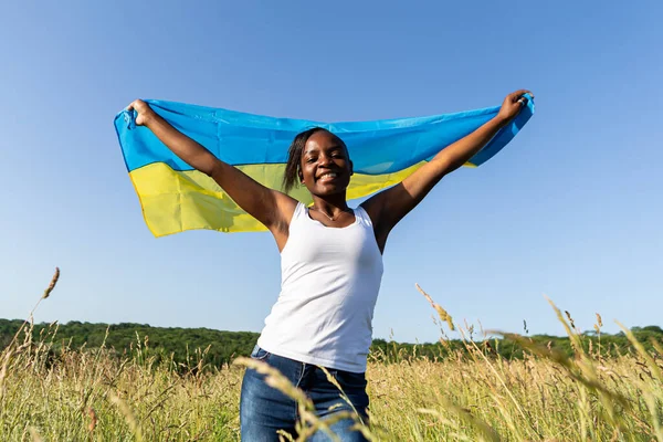 アフリカ系アメリカ人の女性は ウクライナの黄色の青い旗のフラッタ風に手を振って包まれた ウクライナの象徴 ウクライナとのスタンド 国際的な支援と連帯 — ストック写真