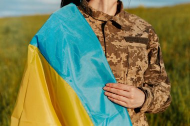 Female soldier dressed in military uniform wrapped in ukrainian flag symbol of independence. Armed Forces of Ukraine. Woman serving in ukrainian army.