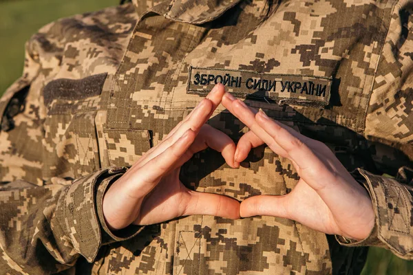 Close up female soldier showing heart love shape sign on velcro patch military uniform. Armed Forces of Ukraine. Woman serving in ukrainian army.