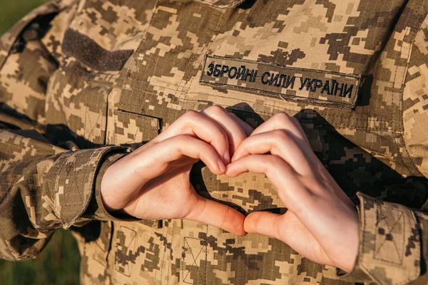 Close up female soldier showing heart love shape sign on velcro patch military uniform. Armed Forces of Ukraine. Woman serving in ukrainian army.