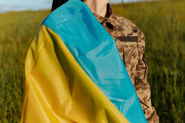 Female soldier dressed in military uniform wrapped in ukrainian flag symbol of independence. Armed Forces of Ukraine. Woman serving in ukrainian army.