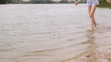 Çıplak kadın bacaklarını nehir boyunca yalınayak koşarken kapat. Deniz kıyısındaki su sıçratan dalgalı ve köpüklü kadın ayakları. Tatildeki kız turist. Hanımefendi banyodan sonra kıyıya çıkın.