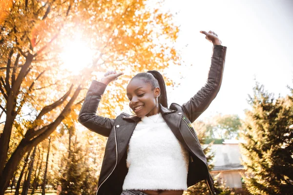 African american woman with dark hair dancing having fun outside autumn city park blur yellow leaves background. Fall time