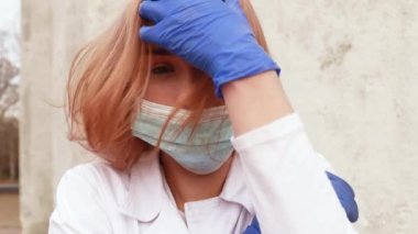 Dirty tired exhausted nurse with ash on face outside hospital infirmary after hard working day or surgery. Doctor woman dressed white medical gown, face mask have a rest due to stress