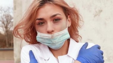 Dirty tired exhausted nurse with ash on face outside hospital infirmary after hard working day or surgery. Doctor woman dressed white medical gown, face mask have a rest due to stress