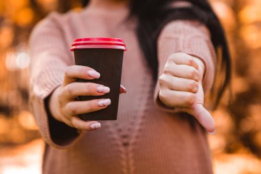 Pregnant woman standing in autumn city park forest, showing dislike thumb down sign gesture, refuses drinking hot beverage coffee tea, prohibition, ban. Fall time. Mother's love, pregnancy concept