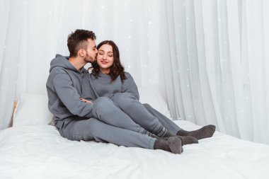 Lovely young romantic couple lying on bed hugging kissing garlands home cosy interior atmosphere New Year Christmas tree decorations holiday party celebrating concept winter evening night