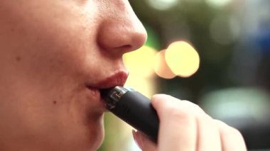 Genç bir kadın dışarıda ve tuz tütün aleti tüttürüyor. Elektronik sigara ısıtıcısı. İçinde sıvı olan duman ve buhar sistemi. Sağlıklı ciğerlere zararlı bir alışkanlık.