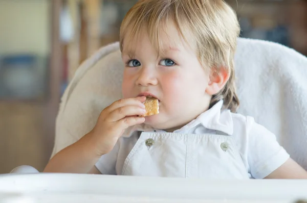 Kleine jongen is zittend aan een tafel en het eten van een cookie — Stockfoto