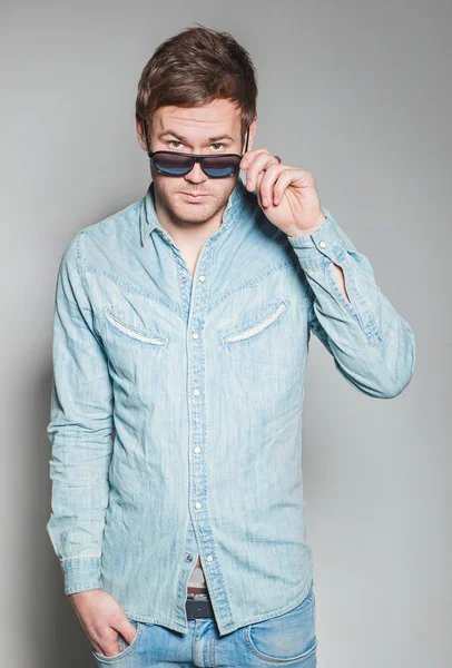 Um cara bonito com óculos e uma camisa jeans — Fotografia de Stock