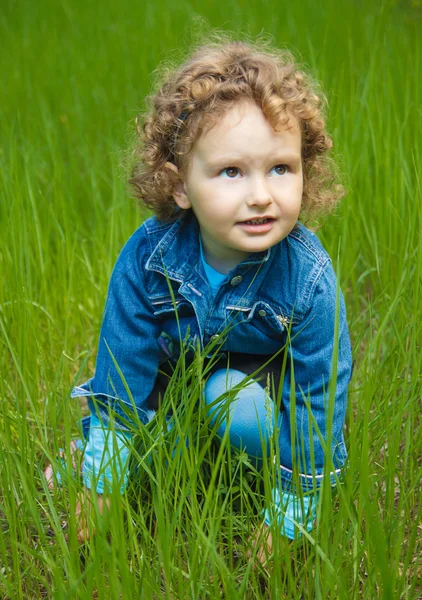 Little curly girl sitting on grass — Stock Photo, Image