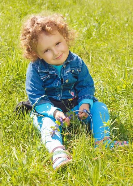 Kleines lockiges Mädchen sitzt auf Gras — Stockfoto