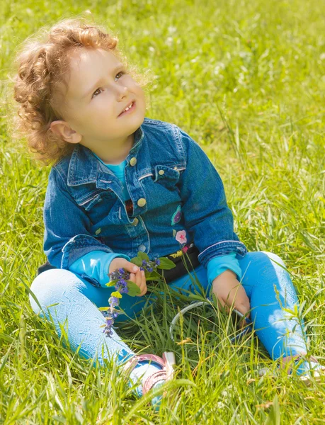 Маленькая кудрявая девочка сидит на траве — стоковое фото