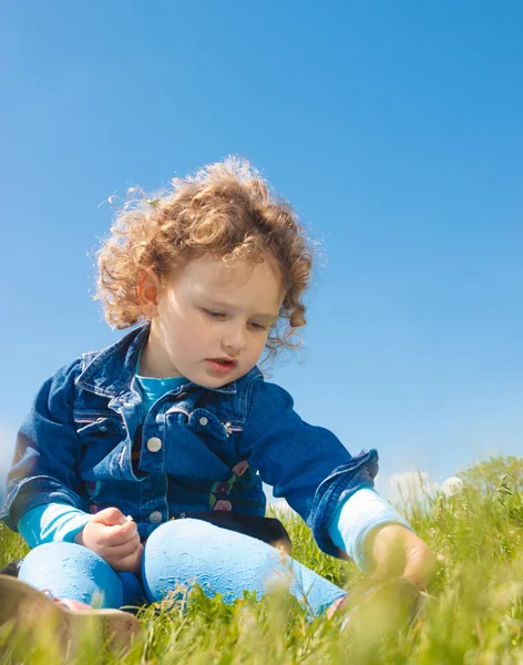 Little curly girl sitting on grass — Stock Photo, Image