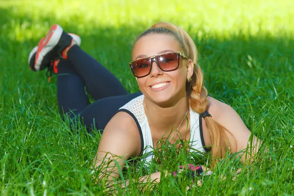 Vacker atletisk flicka leende liggande i gräset — Stockfoto