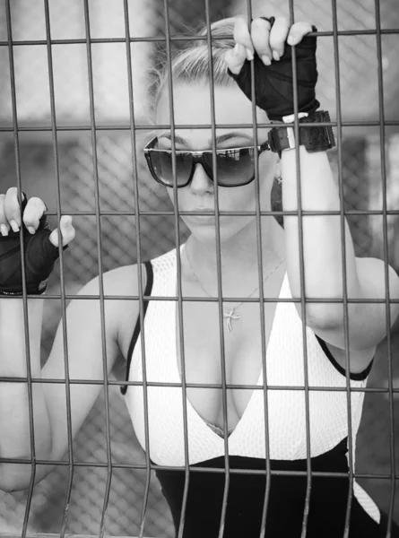 Красивая атлетическая девушка в солнечных очках, смотрящая через решетку — стоковое фото