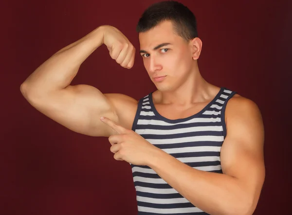 Атлетичный парень в полосатой рубашке показывает свои мышцы — стоковое фото