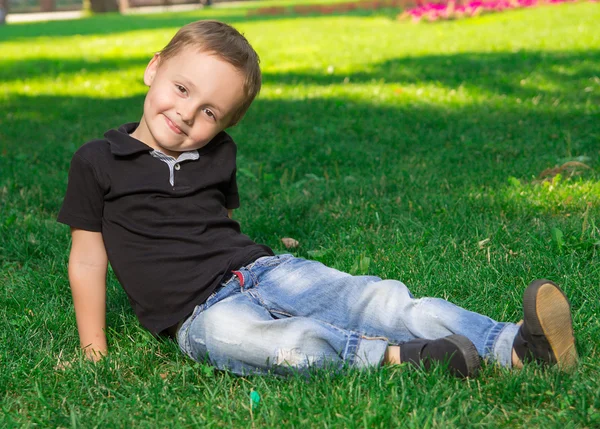 草の上に座っている笑顔の小さな男の子 — ストック写真