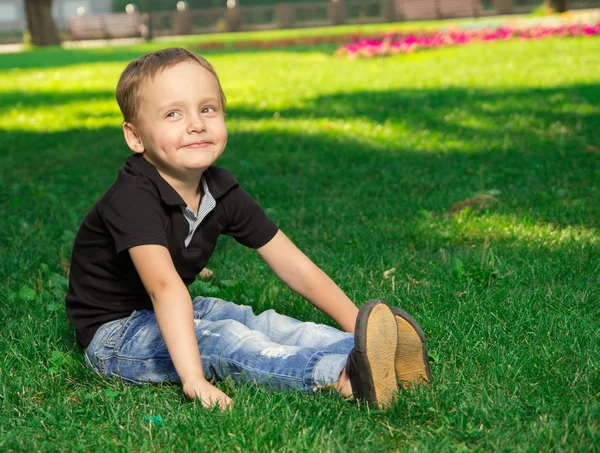 Leende liten pojke sitter på gräset — Stockfoto