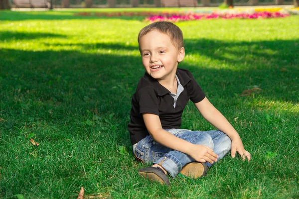Küçük çocuk çimlere oturup gülümseyen — Stok fotoğraf