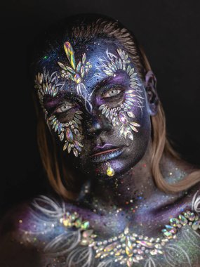 Creative makeup girl with rhinestones and feathers on a dark background